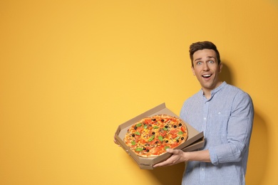 Attractive young man with delicious pizza on color background