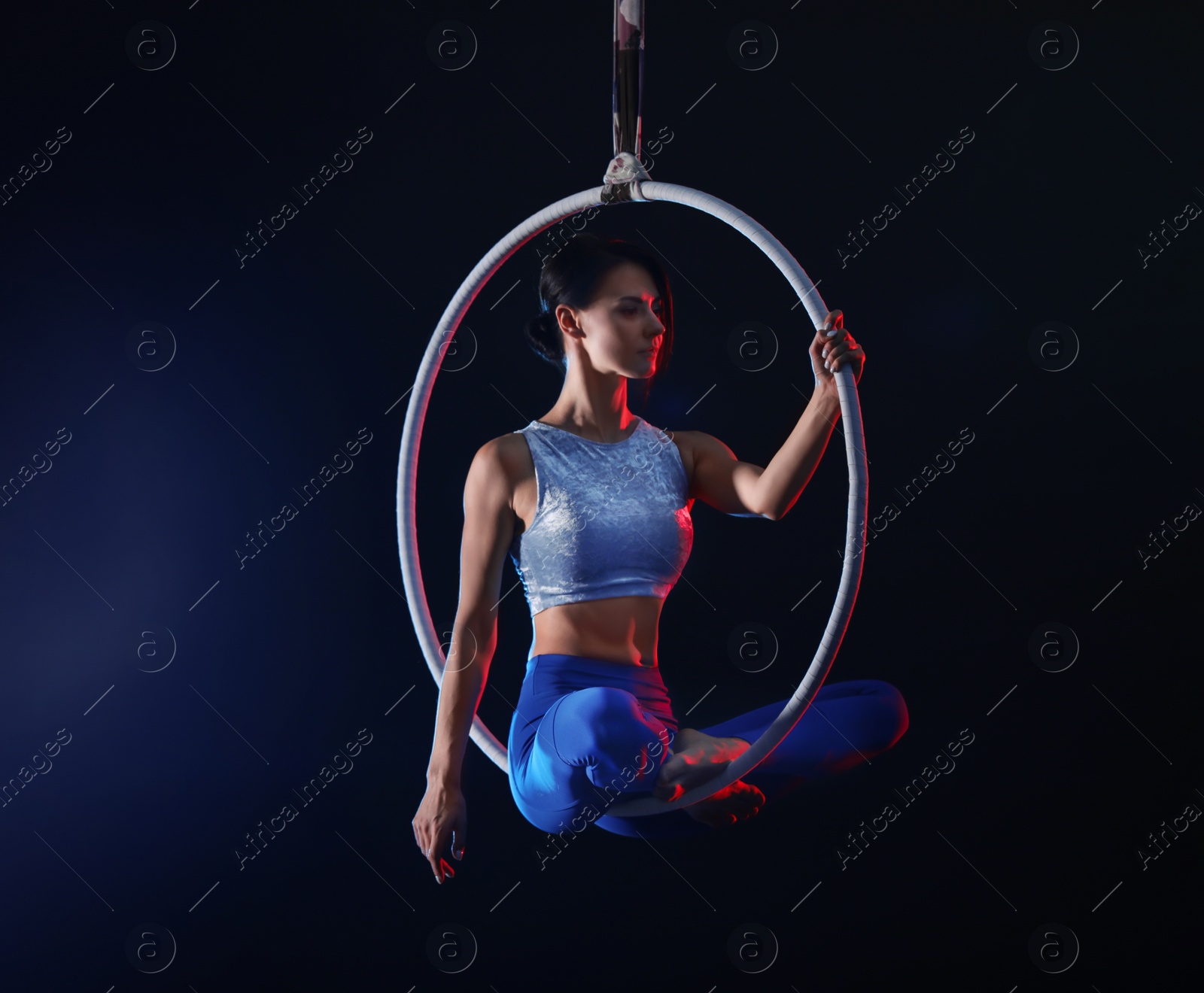 Photo of Young woman performing acrobatic element on aerial ring against dark background. Space for text