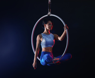 Photo of Young woman performing acrobatic element on aerial ring against dark background. Space for text