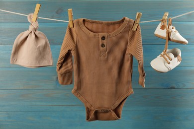 Baby clothes hanging on washing line near light blue wooden wall