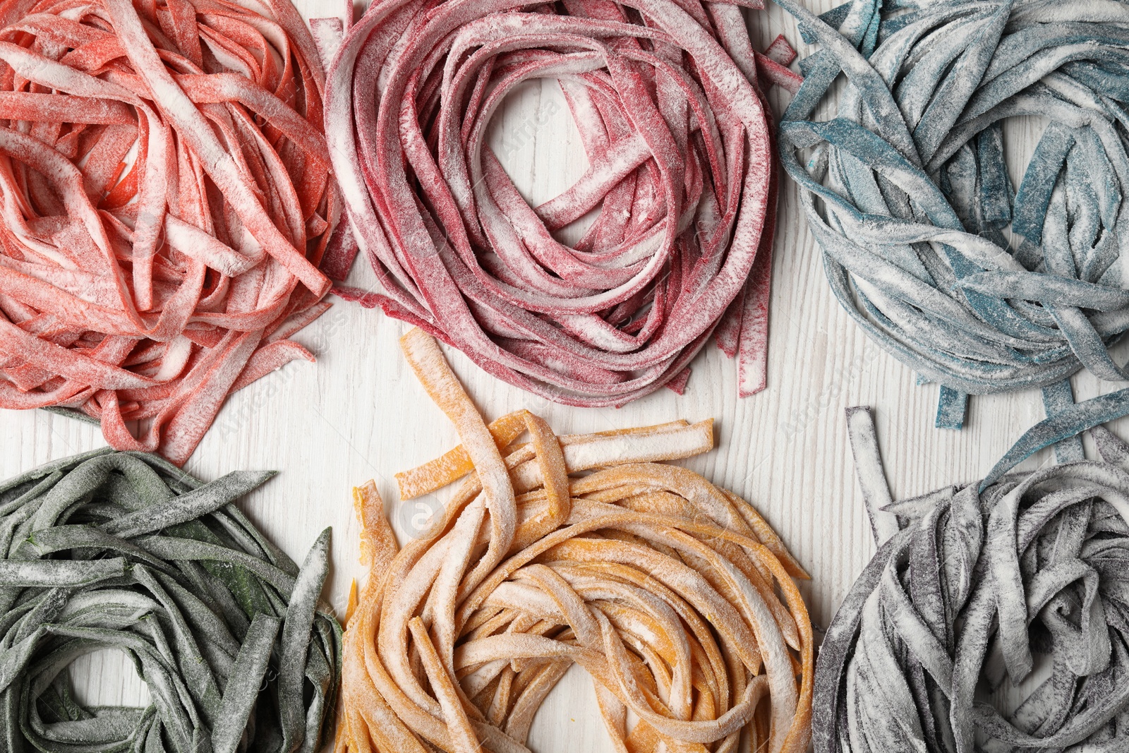 Photo of Rolled pasta painted with different food colorings on white wooden table, flat lay