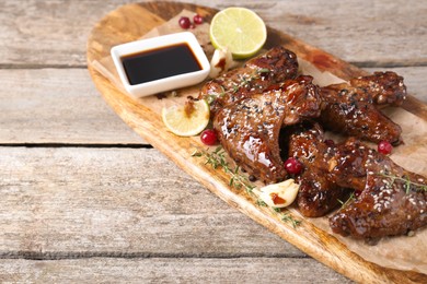 Photo of Tasty chicken wings glazed in soy sauce with garnish on wooden table, space for text