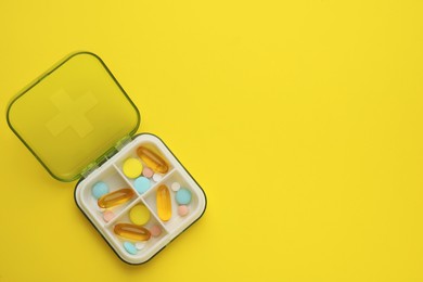 Plastic box with different pills on yellow background, top view. Space for text