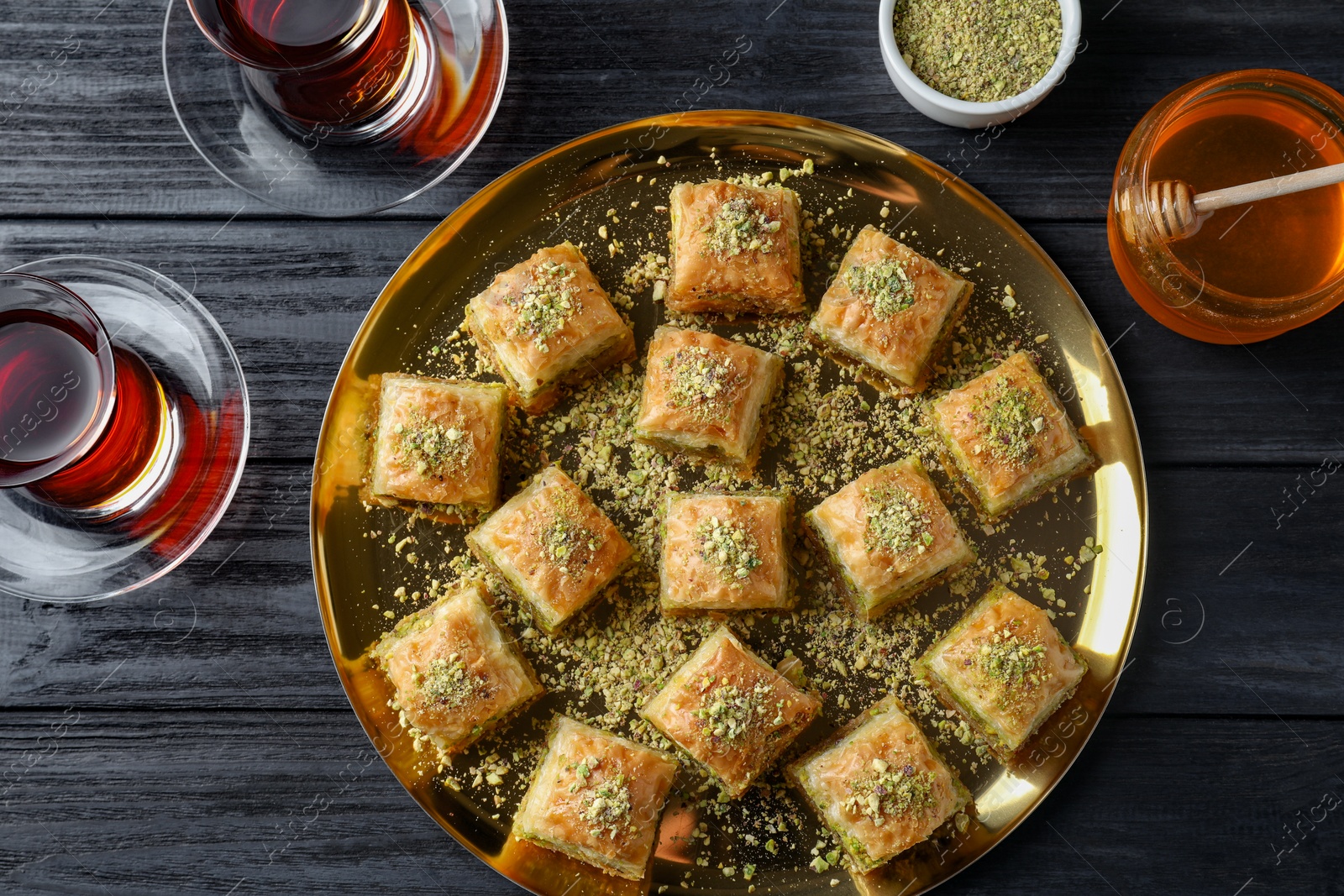 Photo of Delicious fresh baklava with chopped nuts served on black wooden table, flat lay. Eastern sweets