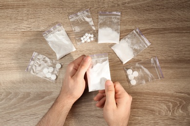 Photo of Man packing drugs in plastic bags at wooden table, top view
