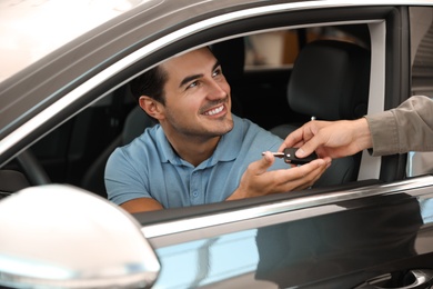 Young salesman giving car key to customer in modern auto dealership, closeup