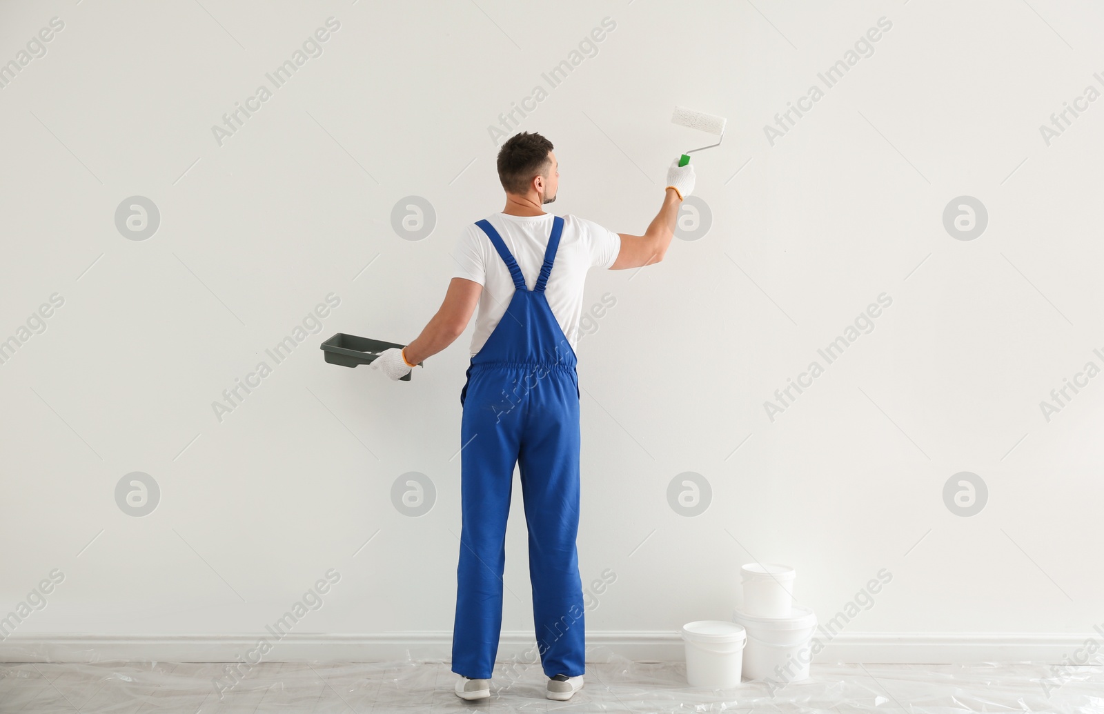 Photo of Man painting wall with white dye indoors, back view