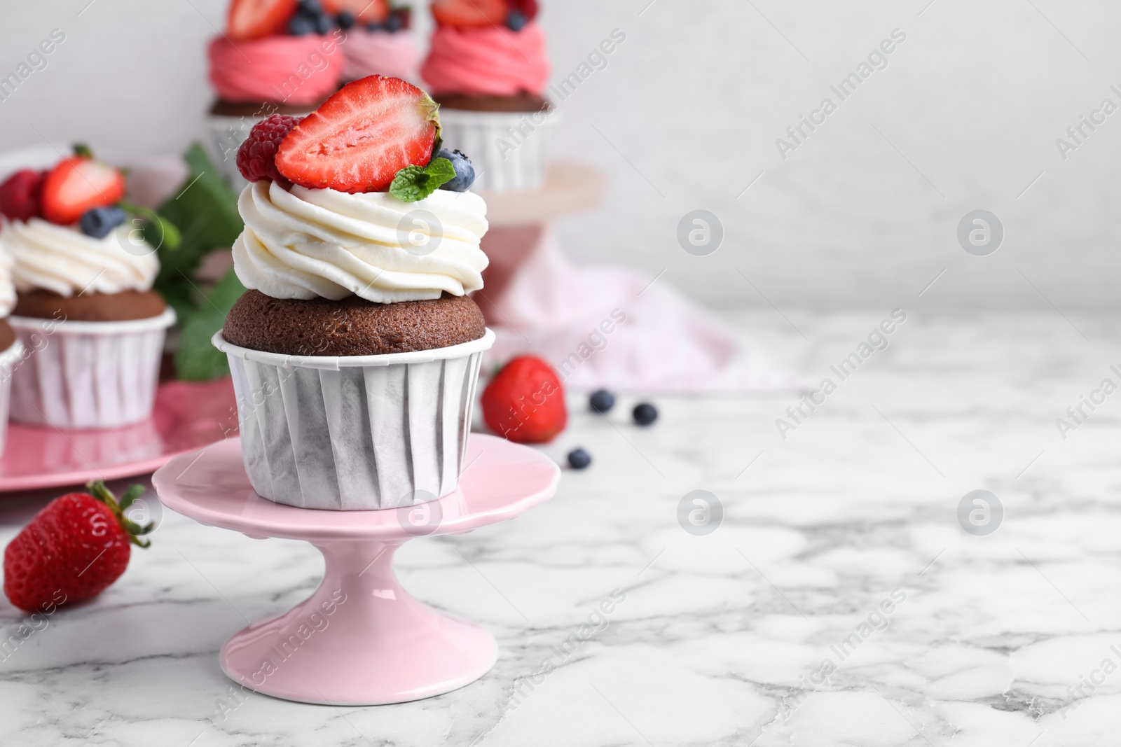 Photo of Delicious cupcake with cream and berries on white marble table, space for text