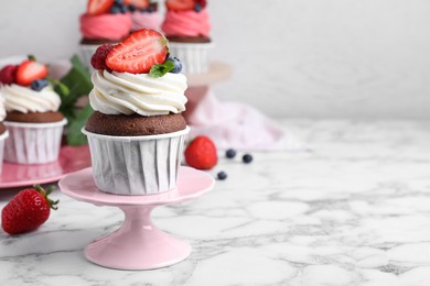 Photo of Delicious cupcake with cream and berries on white marble table, space for text