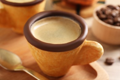 Photo of Delicious edible biscuit cup with espresso and board on table, closeup