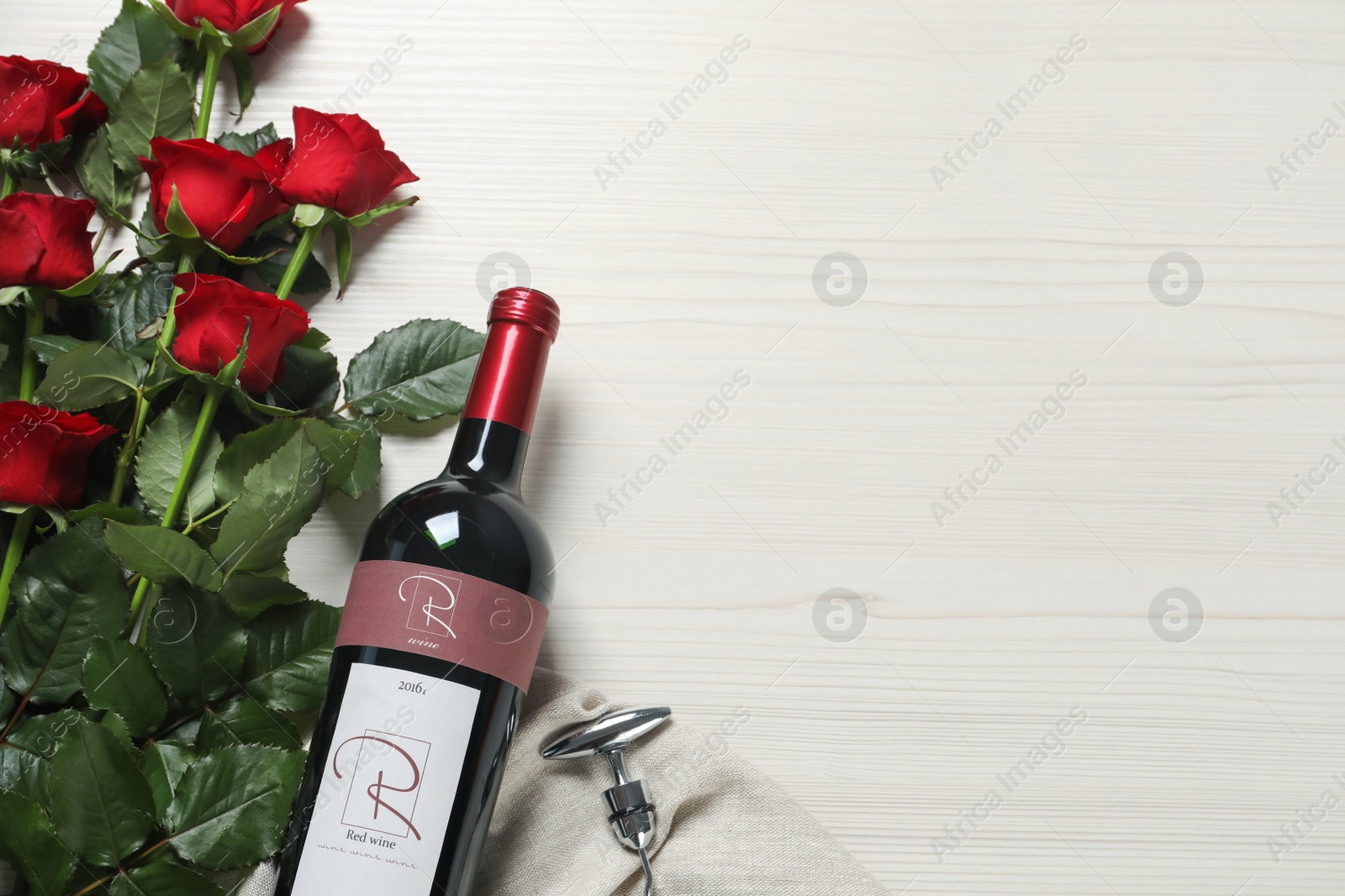 Photo of Bottle of red wine and beautiful roses on white wooden table, flat lay. Space for text