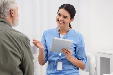 Photo of Smiling nurse with tablet talking to elderly patient in hospital