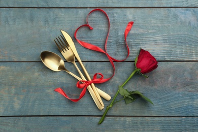 Photo of Beautiful gold cutlery set, flower and red ribbon for Valentine's Day dinner on wooden background, flat lay\