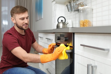 Photo of Young man cleaning oven with rag in kitchen