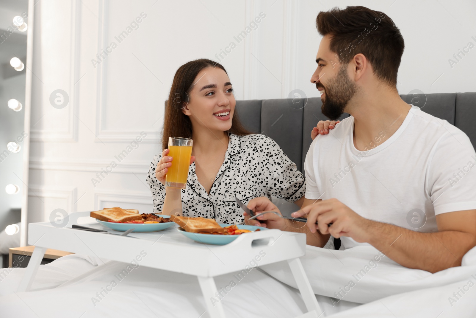 Photo of Happy couple having breakfast on bed at home