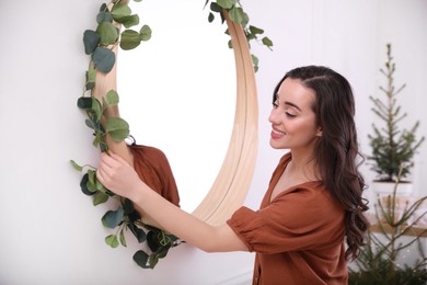 Photo of Woman decorating mirror with eucalyptus branches at home