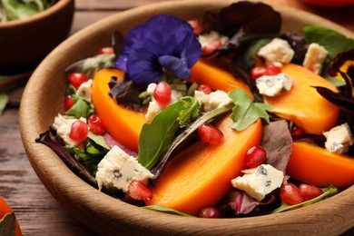 Photo of Delicious persimmon salad with cheese and pomegranate served on wooden table, closeup