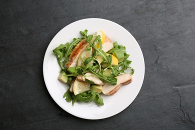 Photo of Delicious salad with chicken, lemon and arugula on black table, top view