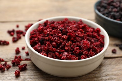 Photo of Bowl of dried red currant berries on wooden table, closeup