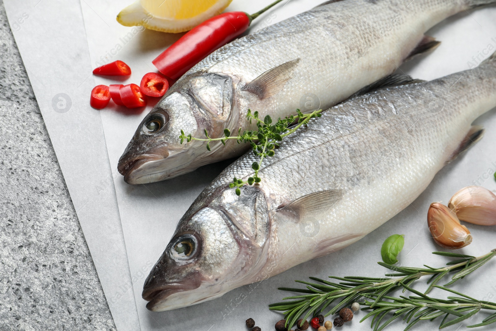 Photo of Sea bass fish and ingredients on grey table, closeup