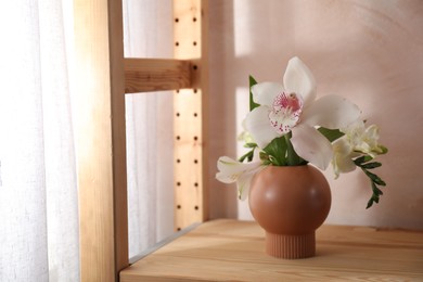 Beautiful flowers in vase on wooden shelf indoors