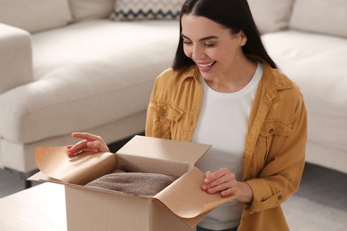 Photo of Happy young woman opening parcel at home. Internet shopping