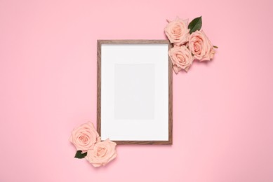 Photo of Empty photo frame and beautiful roses on pink background, flat lay. Mockup for design