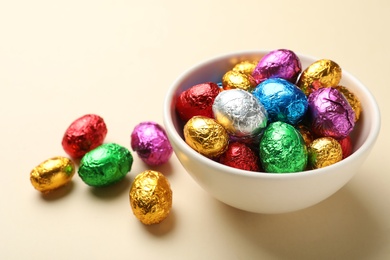 Chocolate eggs wrapped in colorful foil on beige background