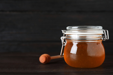 Photo of Jar of organic honey on wooden table against dark background. Space for text