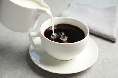 Pouring milk into cup of hot coffee on grey table