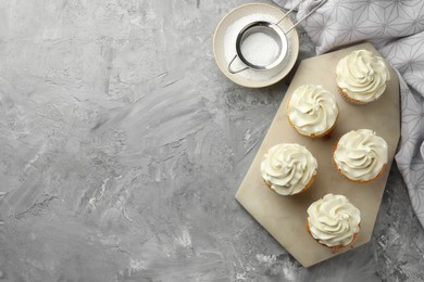 Photo of Tasty cupcakes with vanilla cream on grey table, top view. Space for text