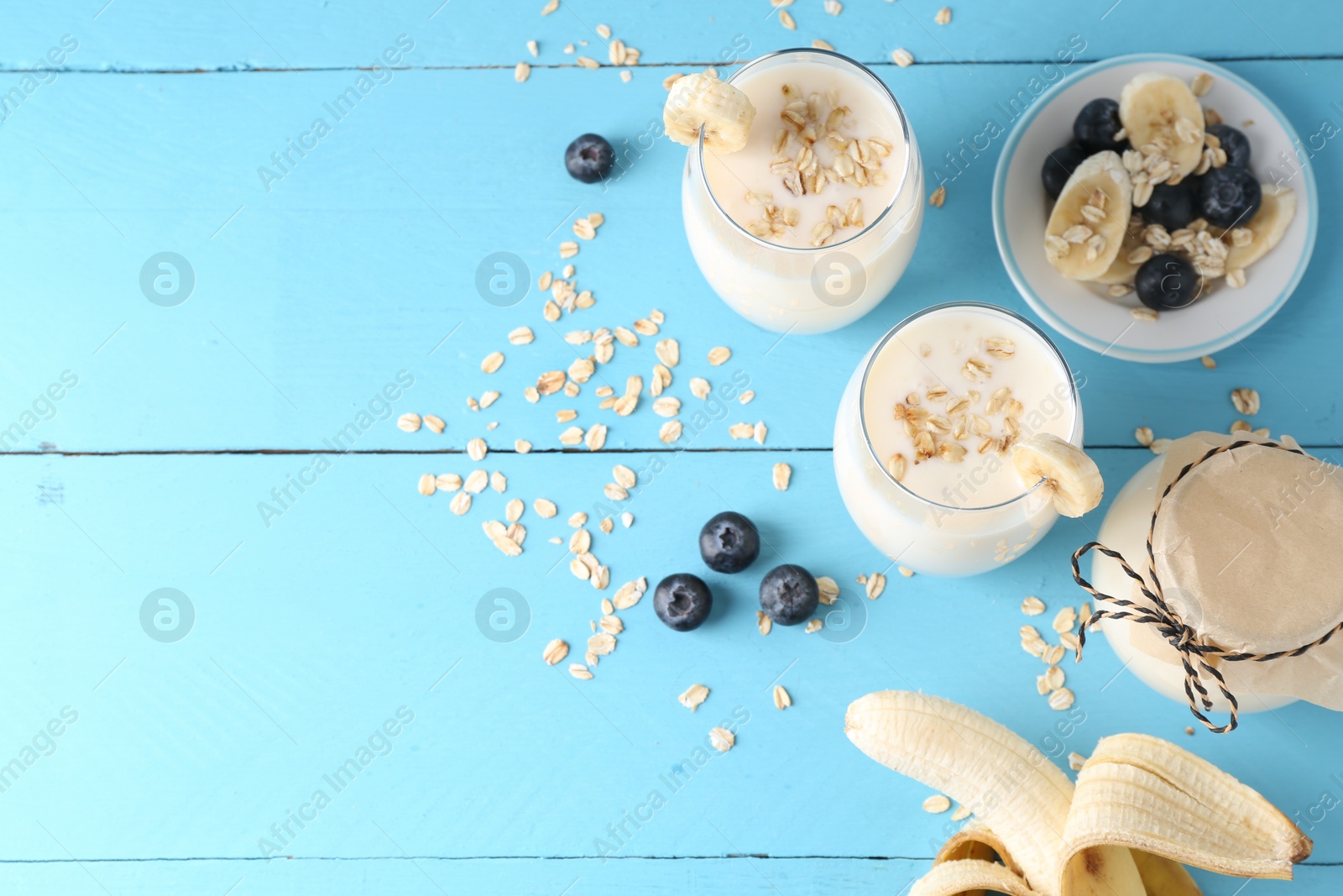 Photo of Tasty yogurt in glasses, oats, banana and blueberries on light blue wooden table, flat lay. Space for text