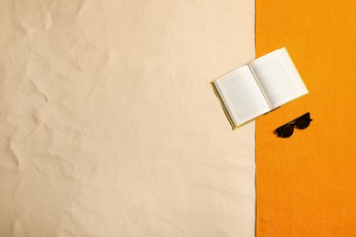 Beach towel, book and sunglasses on sand, flat lay. Space for text