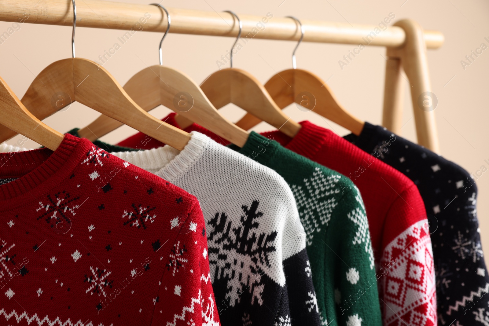 Photo of Rack with different Christmas sweaters on beige background, closeup