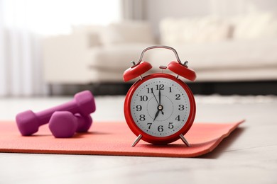 Photo of Alarm clock, yoga mat and dumbbells on wooden floor indoors. Morning exercise