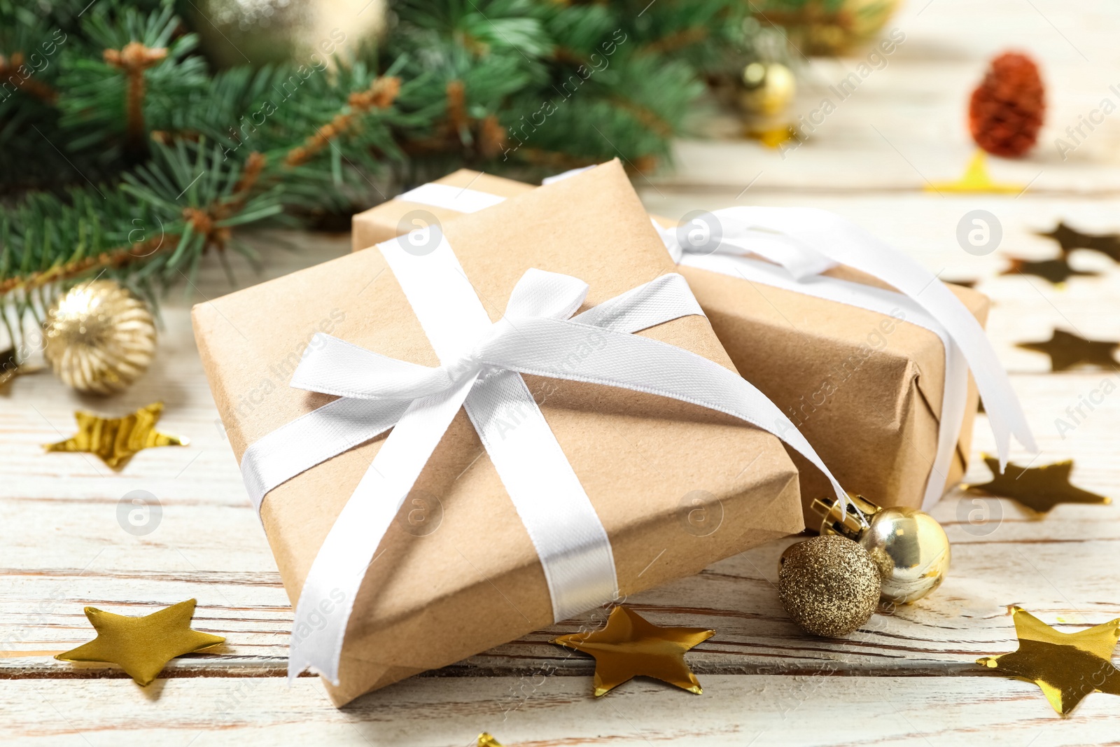 Photo of Gift boxes, fir branches, Christmas balls and shiny confetti on white wooden table