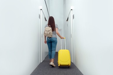 Woman with backpack and suitcase walking along hostel corridor, back view