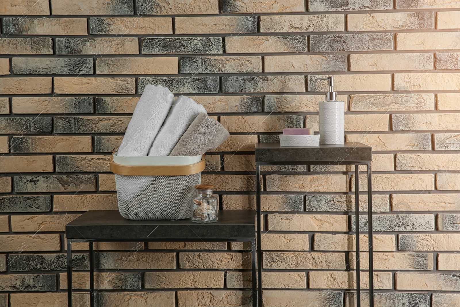 Photo of Tables with soap, bottle of shampoo and towels near brick wall