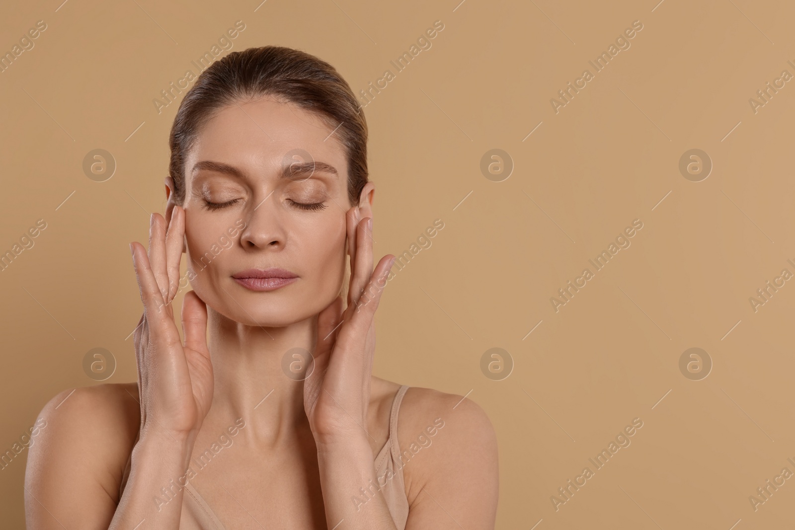 Photo of Woman massaging her face on beige background. Space for text