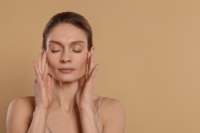 Woman massaging her face on beige background. Space for text