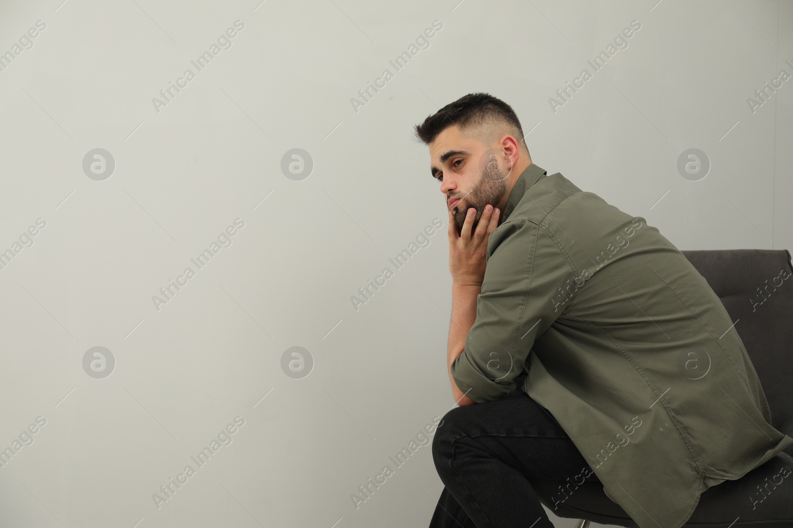 Photo of Sad man sitting near light grey wall. Space for text