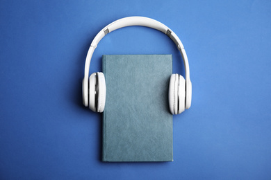 Photo of Book and modern headphones on blue background, top view