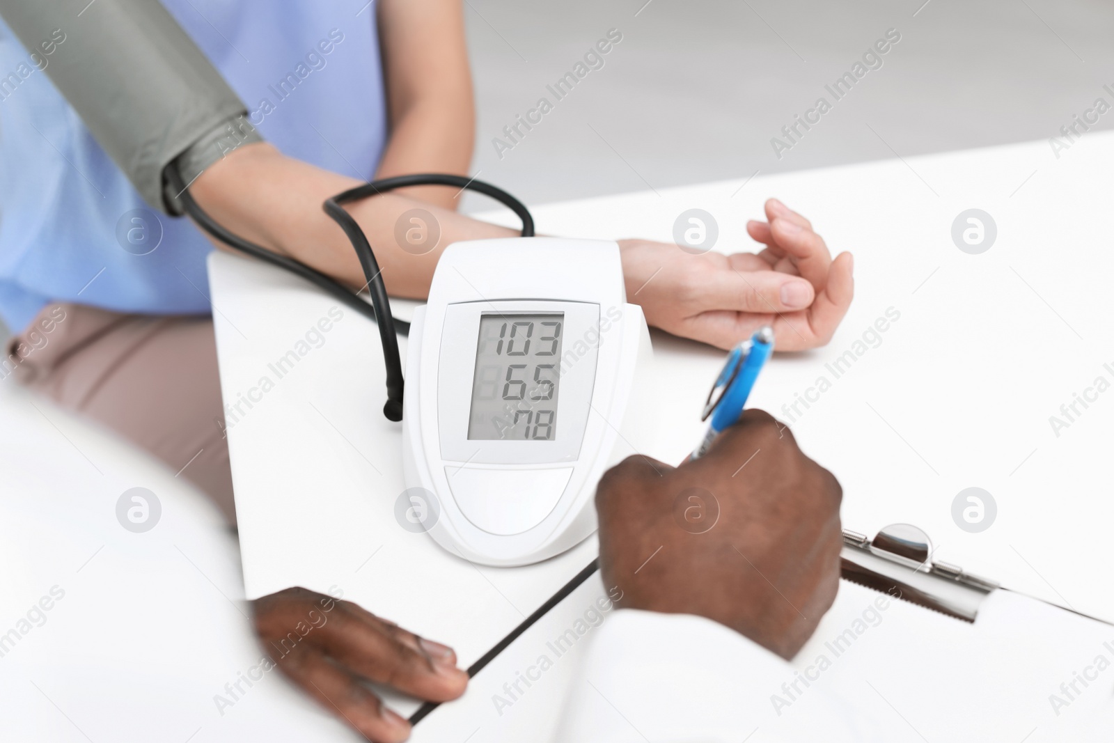 Photo of Young African-American doctor checking patient's blood pressure in hospital