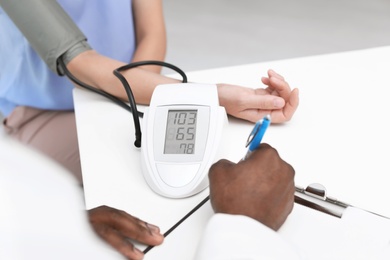 Young African-American doctor checking patient's blood pressure in hospital