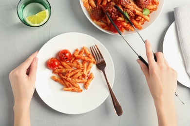 Woman putting meatballs into pasta with tomato sauce at table, closeup