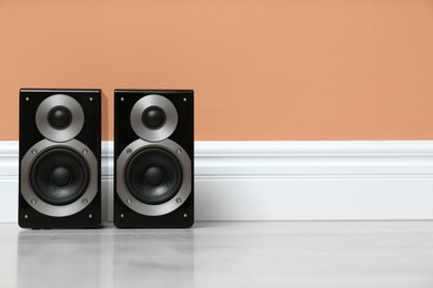 Modern powerful audio speakers on floor near orange wall. Space for text