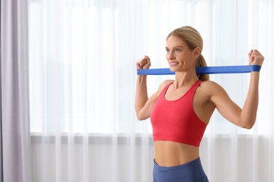 Photo of Fit woman doing exercise with fitness elastic band indoors. Space for text