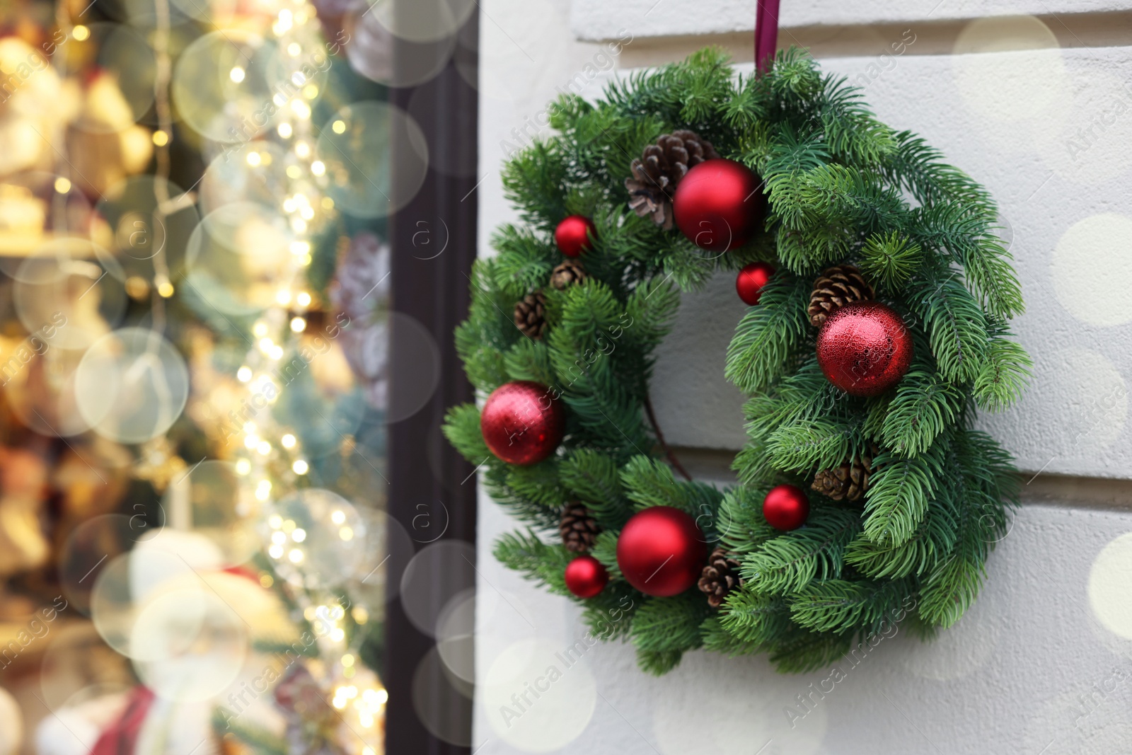 Photo of Beautiful Christmas wreath hanging on white building wall outdoors, space for text