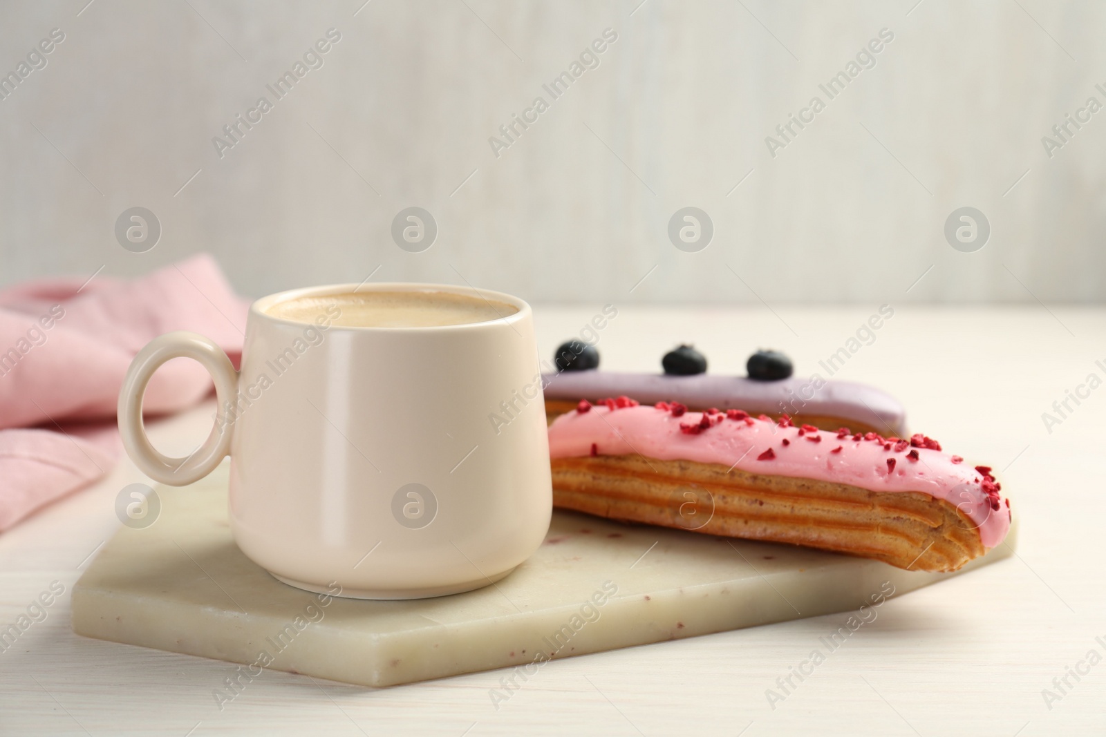 Photo of Cup of coffee and delicious eclairs covered with glaze on white wooden table