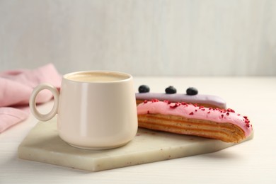 Cup of coffee and delicious eclairs covered with glaze on white wooden table